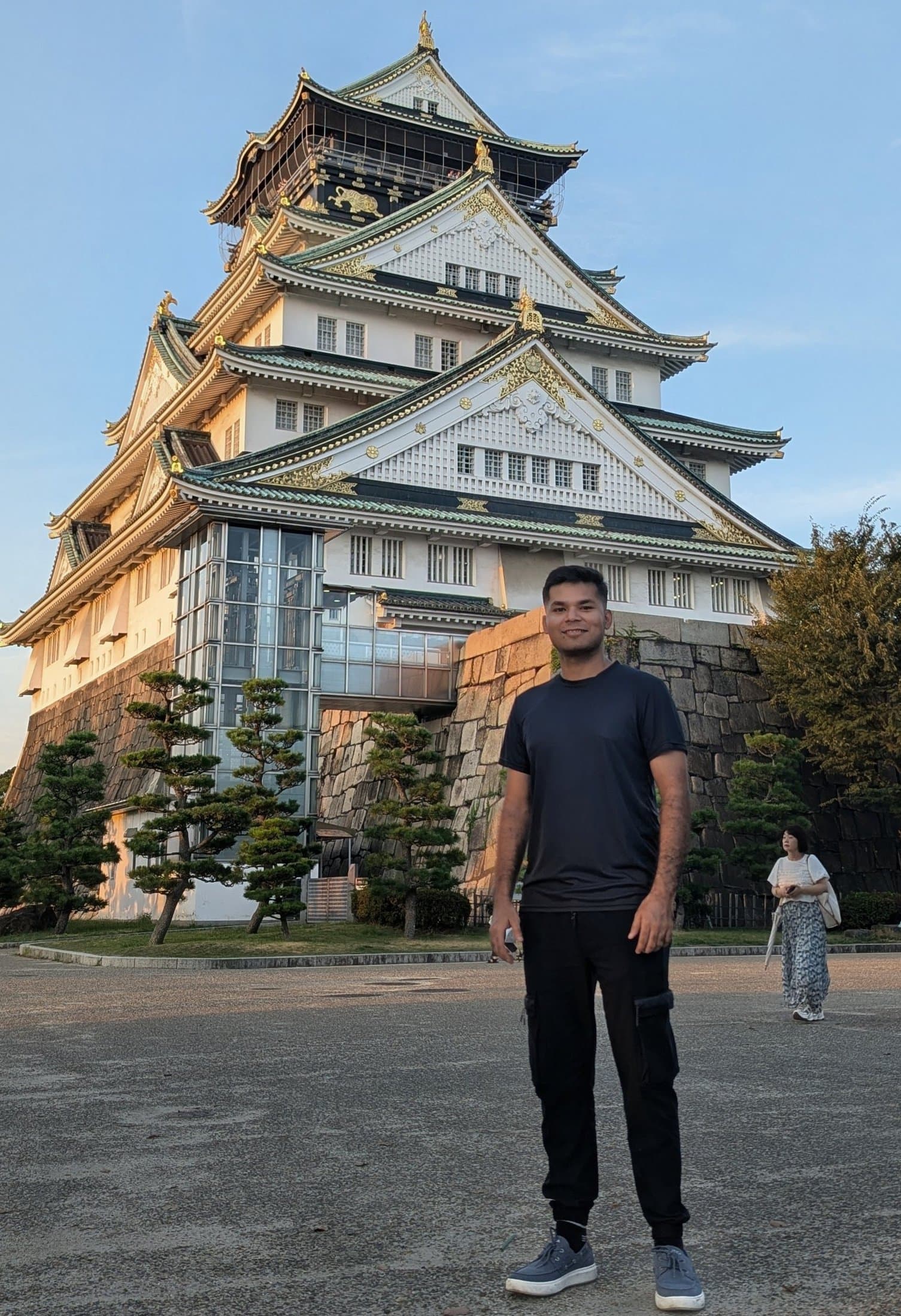 Shivam standing in front of Osaka Castle, its layered green-and-gold roofs visible against a clear sky.