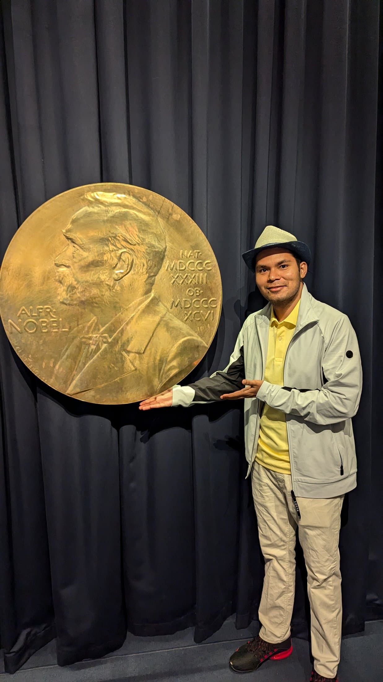 Shivam posing beside a large replica Nobel Prize medal on display inside the Nobel Prize Museum in Stockholm.